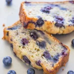 Blueberry Banana Zucchini Bread on a wooden board with blueberries and zucchini