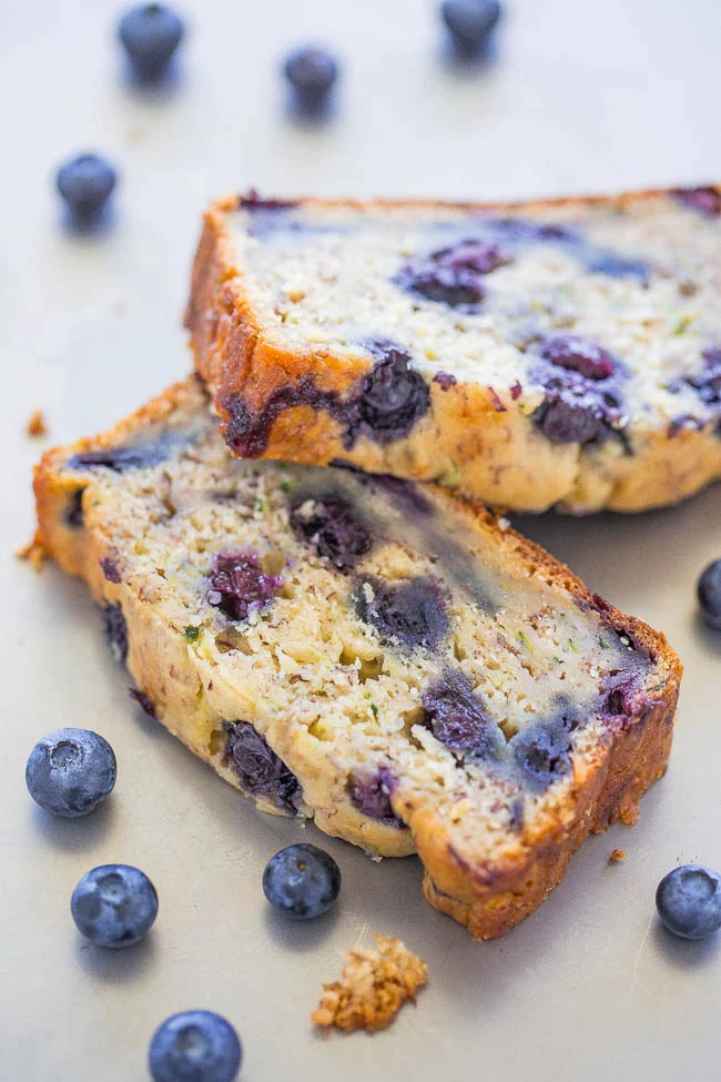 Blueberry Banana Zucchini Bread on a wooden board with blueberries and zucchini