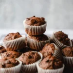 Healthy & Moist Chocolate Zucchini Muffins 3 Moist chocolate zucchini muffins topped with chocolate chips on a white plate.