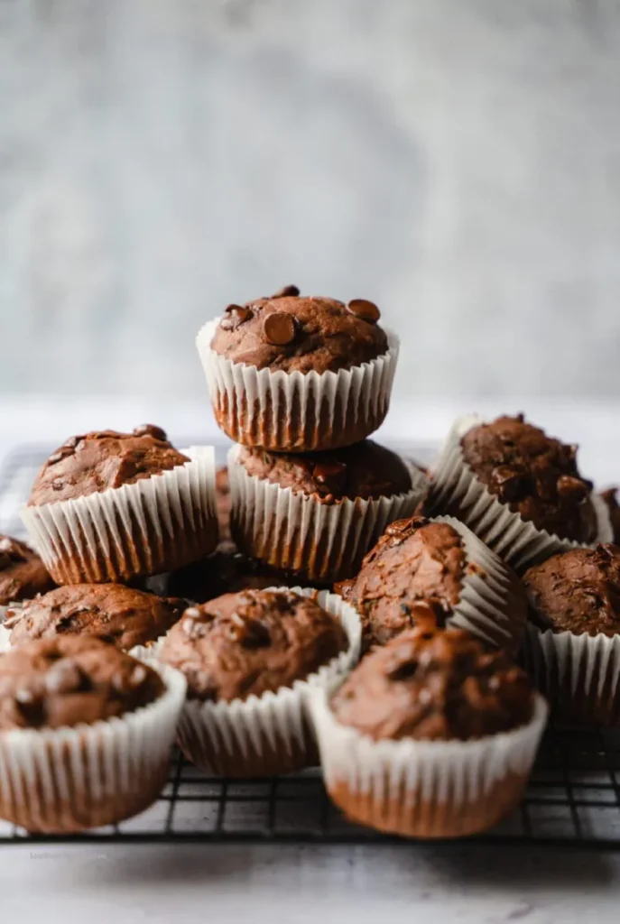 Moist chocolate zucchini muffins topped with chocolate chips on a white plate.