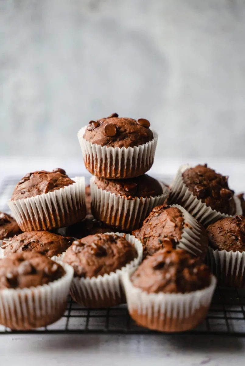 Moist chocolate zucchini muffins topped with chocolate chips on a white plate.